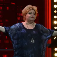 Wokalistka jazzowa imieniem Szafran, z rozłożonymi ramionami, w ciemnej, wzorzystej sukience, na tle czerwonych świateł.