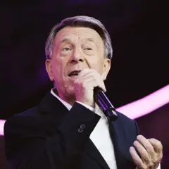 Wojciech Gąssowski śpiewa "Gdzie się podziały tamte prywatki". Artysta w czarnym garniturze i białej koszuli, z mikrofonem w dłoni, na tle fioletowych świateł.