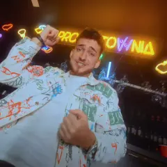 Hej, co zrobiłaś? Jaka głupia byłaś! Młody mężczyzna w kolorowej kurtce tańczy na tle neonów i baru.