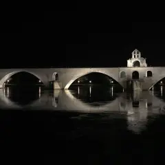 Nocna panorama na moście w Avignon. Kamienne łuki odbijają się w spokojnej wodzie rzeki Rodan.