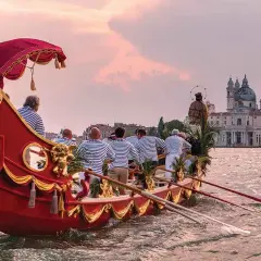 Wenecka barkarola z pasażerami w strojach marynarskich płynie w kierunku bazyliki Santa Maria della Salute.