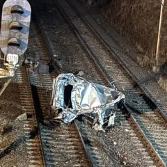 Zmiażdżony samochód na torach kolejowych, obok semafora. Wygląda jakby ktoś przejechał przez ten samochód.