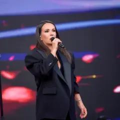 Kasia Kowalska w czarnej marynarce śpiewa na scenie, wykonując swoje utwory.