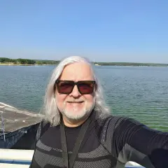Ira wokalista w okularach przeciwsłonecznych pozuje do selfie nad jeziorem.
