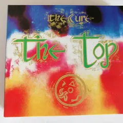 Okładka albumu "The Top" zespołu The Cure. Kolorowe, psychodeliczne tło z zielonym napisem "the Top" i złotym logo zespołu.