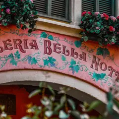 Różowa fasada Pizzerii Bella Notte ozdobiona winoroślą i kwiatami.
