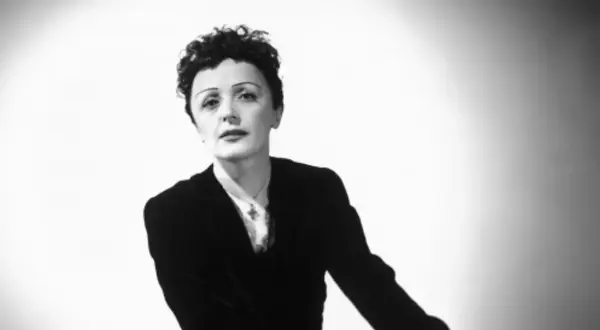 Edith Piaf, ikona francuskiej piosenki, w czarnym żakiecie i z charakterystyczną fryzurą. Jej piosenki wciąż poruszają serca.