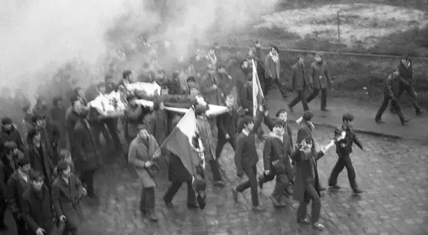 Tłum niesie nosze z ciałem, dym unosi się w powietrzu. Janek Wiśniewski padł, a jego towarzysze idą dalej.