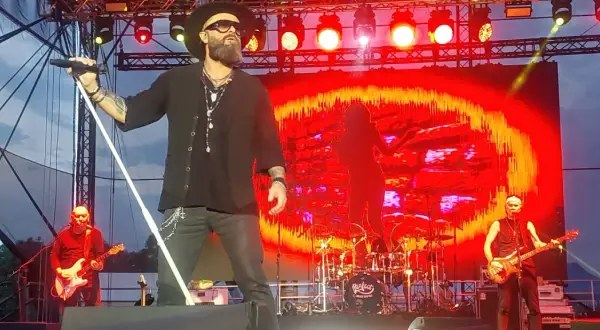 Koncert zespołu Perfect. Wokalista śpiewa, a na scenie widać gitarzystów i perkusję. Tło to czerwono-żółte wizualizacje. Autobiografia akordy.