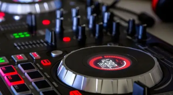 Zbliżenie na konsolę DJ-ską z podświetlanymi przyciskami i wyświetlaczem.
