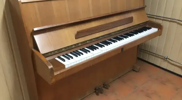 Drewniane pianino pionowe z klawiaturą. Zastanawiasz się, ile waży pianino? To instrument, który wymaga siły do przeniesienia.