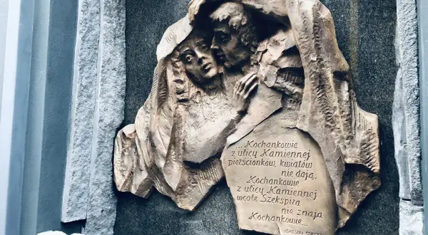 Rzeźba "Kochankowie z ulicy Kamiennej" przedstawia przytulonych ludzi pod płaszczem. Cytat Agnieszki Osieckiej mówi o miłości.