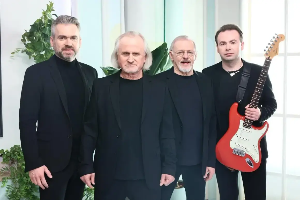 Czterech mężczyzn w czarnych strojach. Jeden z nich trzyma czerwoną gitarę, gotową do wykonania utworów.