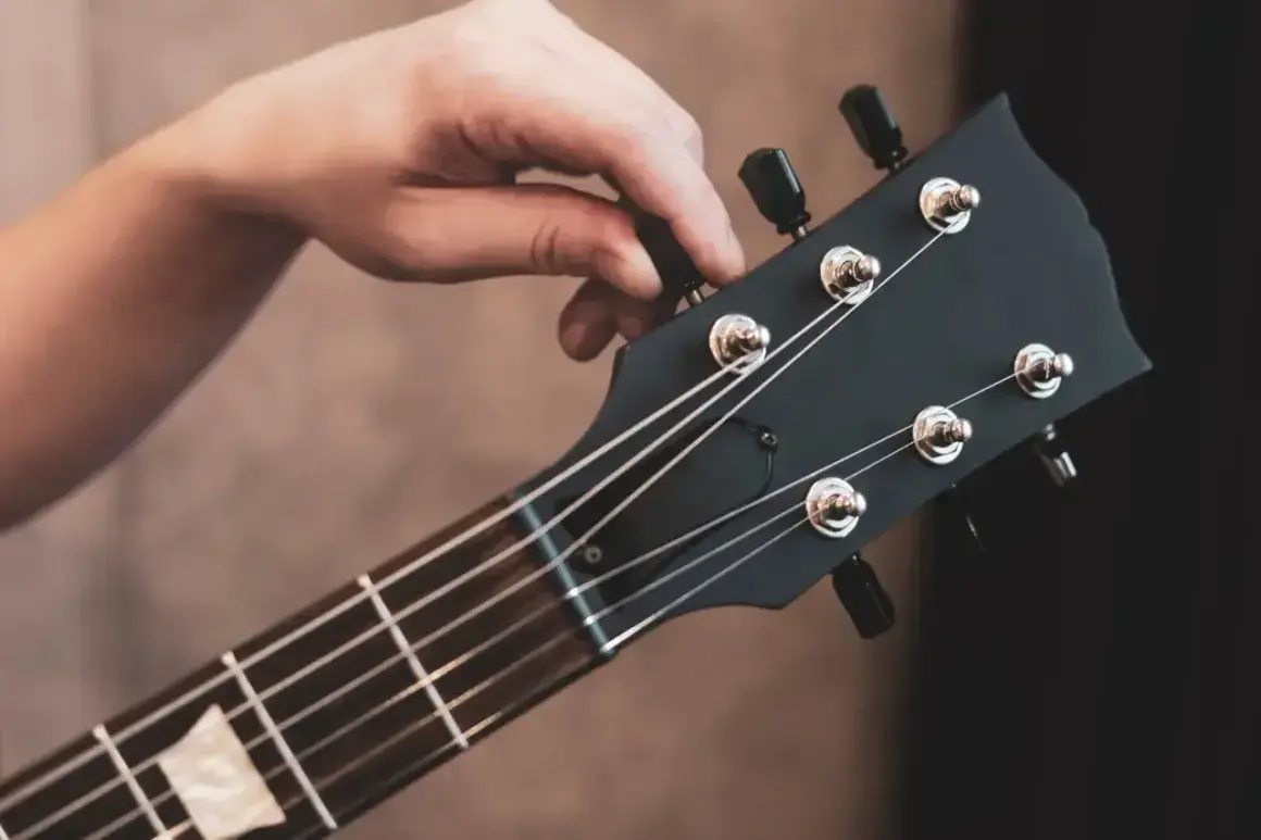 Dłoń kręci kluczem, by nastroić gitarę. Precyzyjne ruchy zapewniają idealne brzmienie.