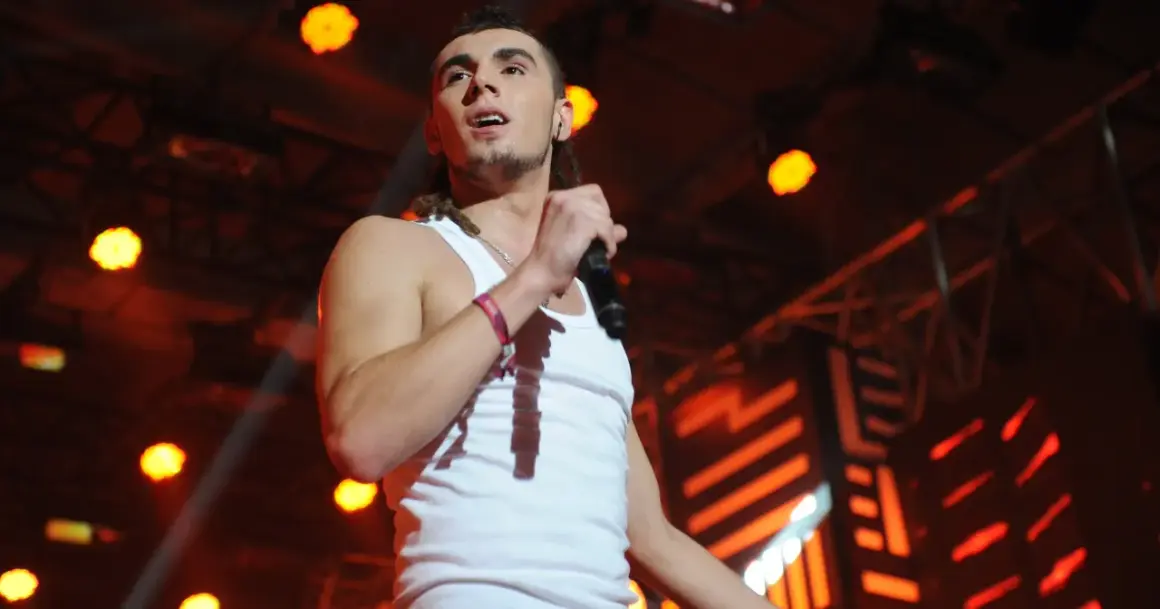 Kamil, piosenkarz reggae, śpiewa do mikrofonu na scenie oświetlonej pomarańczowymi światłami.
