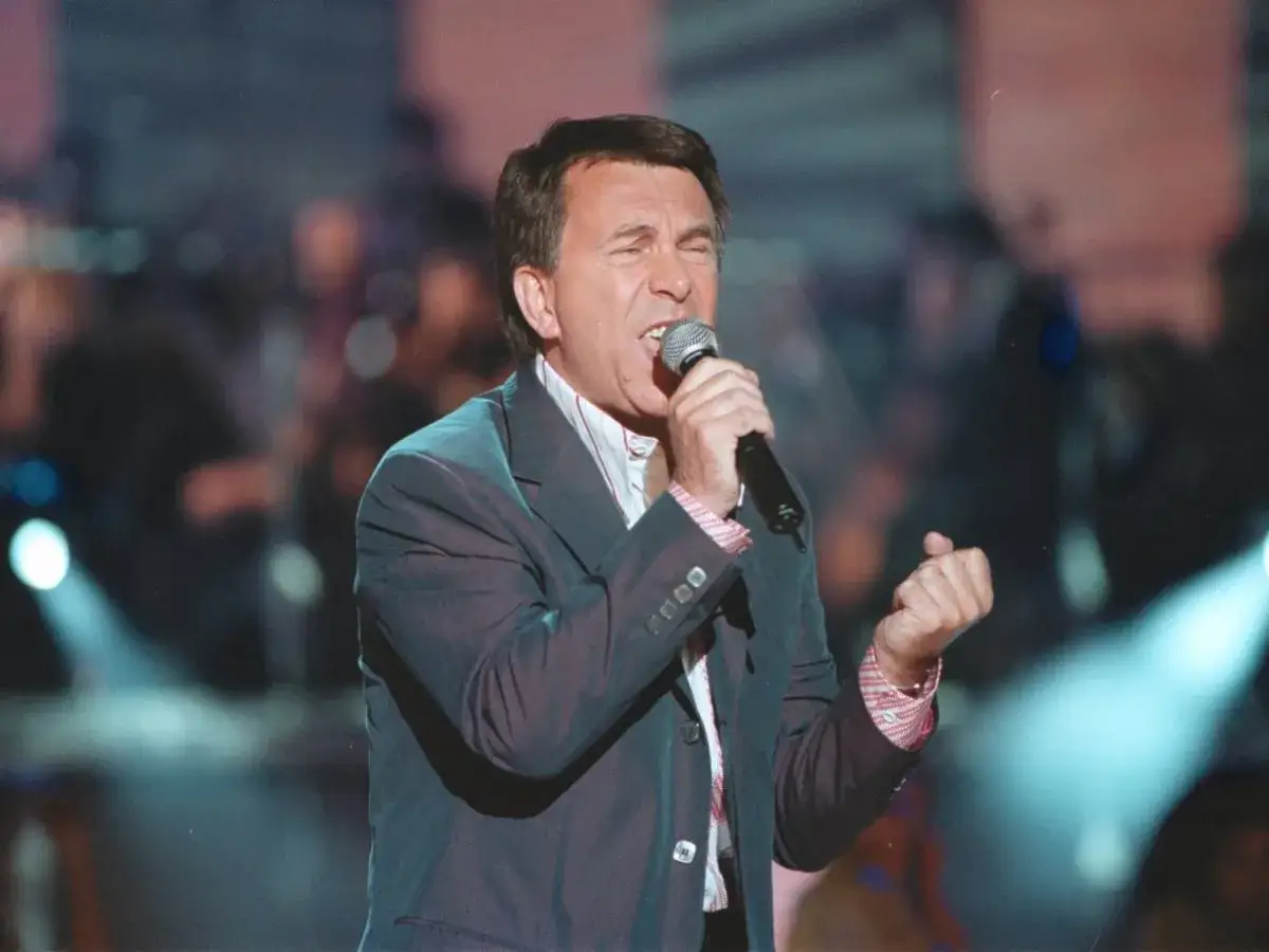 Wojciech Gąsowski śpiewa z pasją, trzymając mikrofon. Jego oczy są zamknięte, a ręka zaciśnięta w pięść.