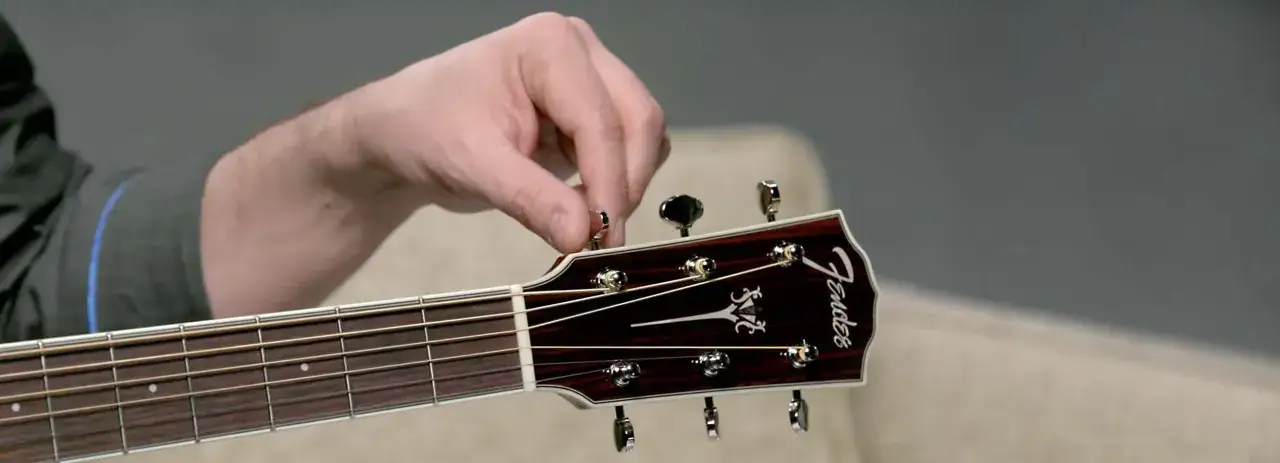 Dłoń kręci kluczem przy główce gitary Fender, pokazując jak nastroić gitarę.