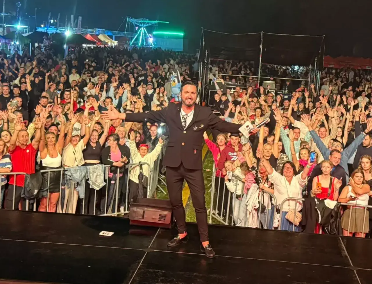 Gwiazda disco polo w garniturze pozdrawia rozentuzjazmowany tłum na koncercie.
