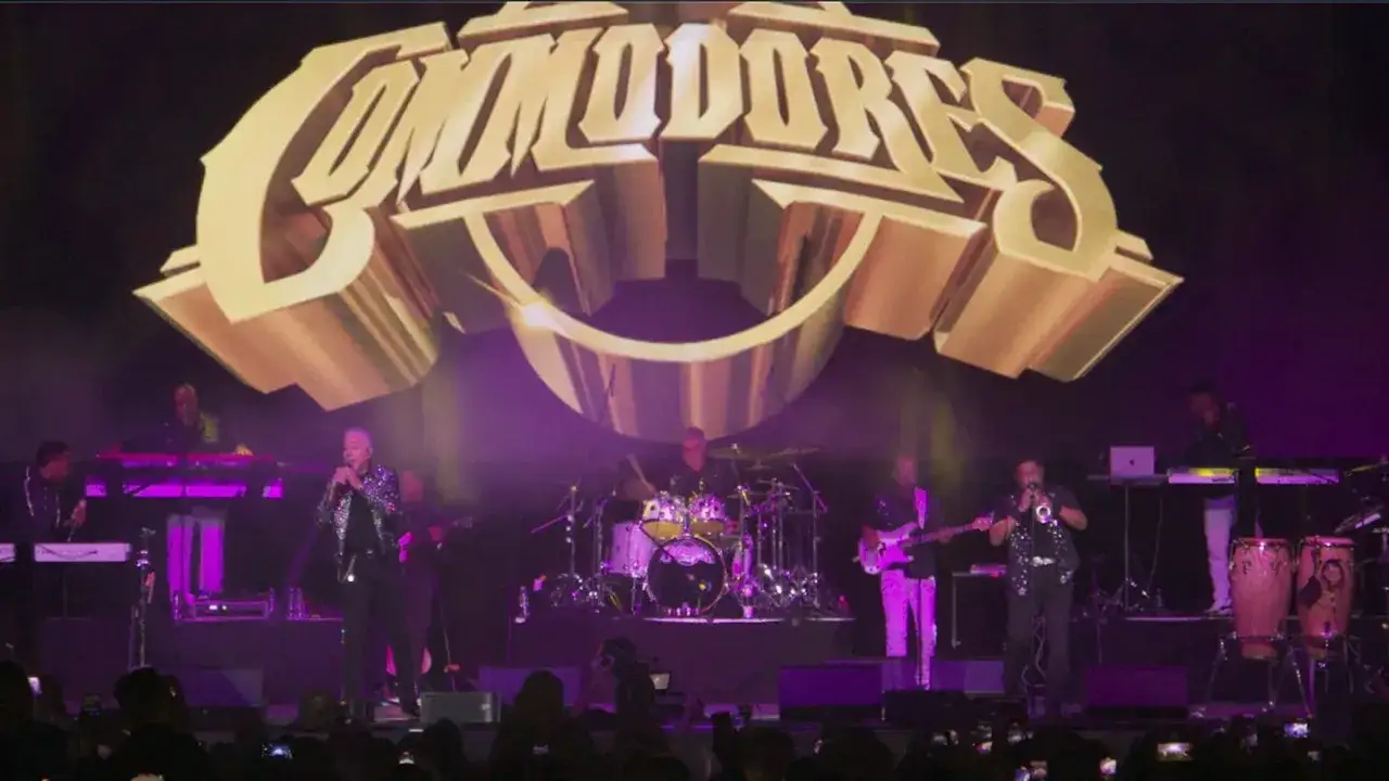 Koncert zespołu Commodores, gdzie każdy dźwięk jest easy like Sunday morning. Wokalista śpiewa, a zespół gra na instrumentach pod złotym logo.