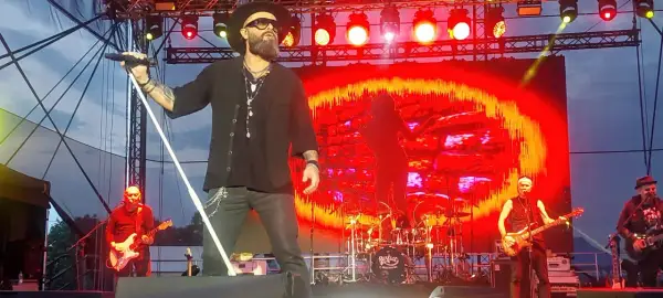 Koncert zespołu Perfect. Wokalista śpiewa, a na scenie widać gitarzystów i perkusję. Tło to czerwono-żółte wizualizacje. Autobiografia akordy.
