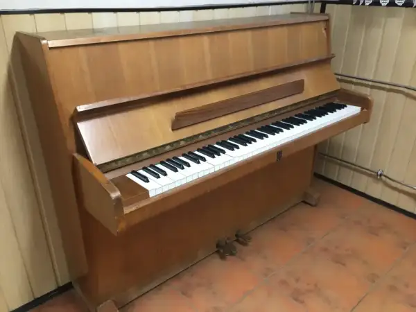 Drewniane pianino pionowe z klawiaturą. Zastanawiasz się, ile waży pianino? To instrument, który wymaga siły do przeniesienia.