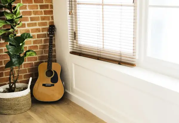 Akustyczna gitara obok ceglanej ściany i rośliny w koszu. Idealne miejsce na proste piosenki na gitarę dla dzieci.